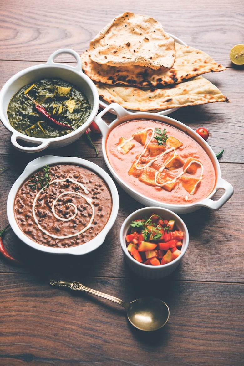 bowls of desi food dishes (indian cuisine) on a wooden table with naan bread