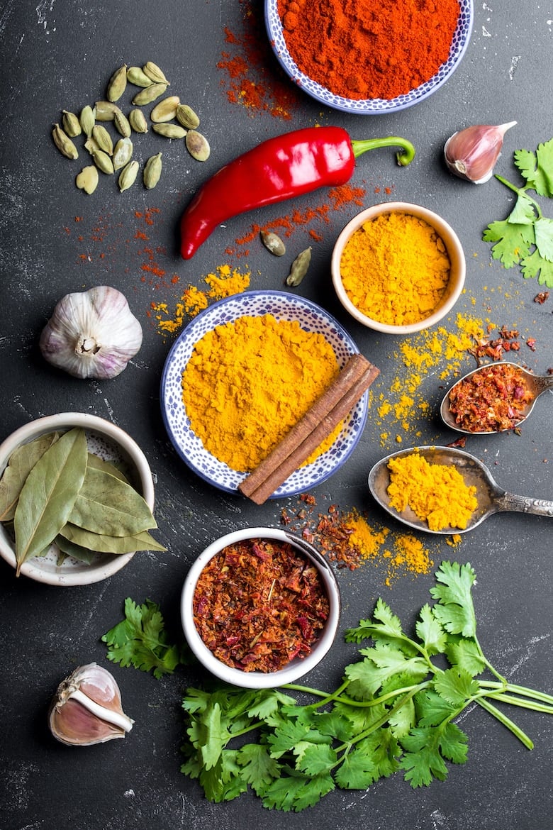 Set of Indian food cooking ingredients. Traditional Indian assorted spices and herbs. Curry, turmeric, cardamom, garlic, pepper, cilantro, cinnamon. Preparing exotic meal. Top view, close up