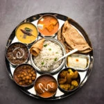 An Indian food platter of a variety of desi food dishes arranged in a circular fashion.
