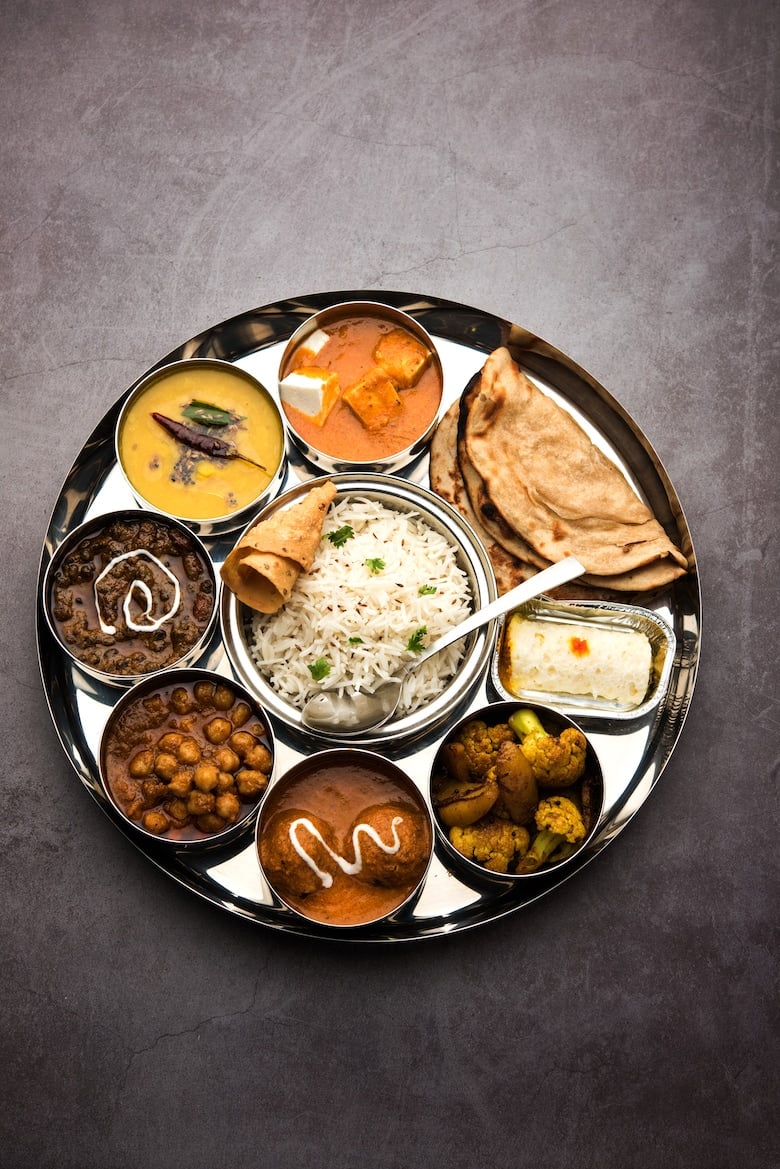 An Indian food platter of a variety of desi food dishes arranged in a circular fashion.