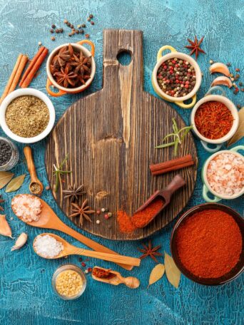 Dry colorful spices and condiments anise, paprika, saffron, pepper, salt, bay leaf, cinnamon in small bowls on blue background
