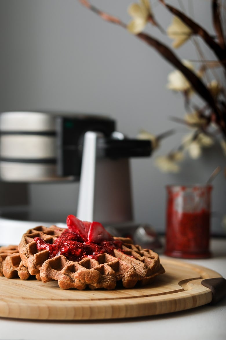 Strawberry chia jam topped on a brown waffle with a waffle maker in the background