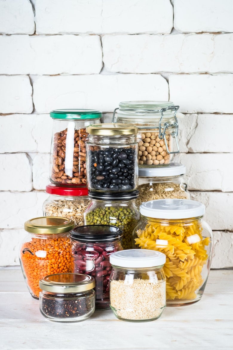 Cereals, Legumes, and beans in glass jars on white kitchen table. Rice, corn, quinoa, beans, soy, lentils, mache, pasta. Healthy food for cooking.
