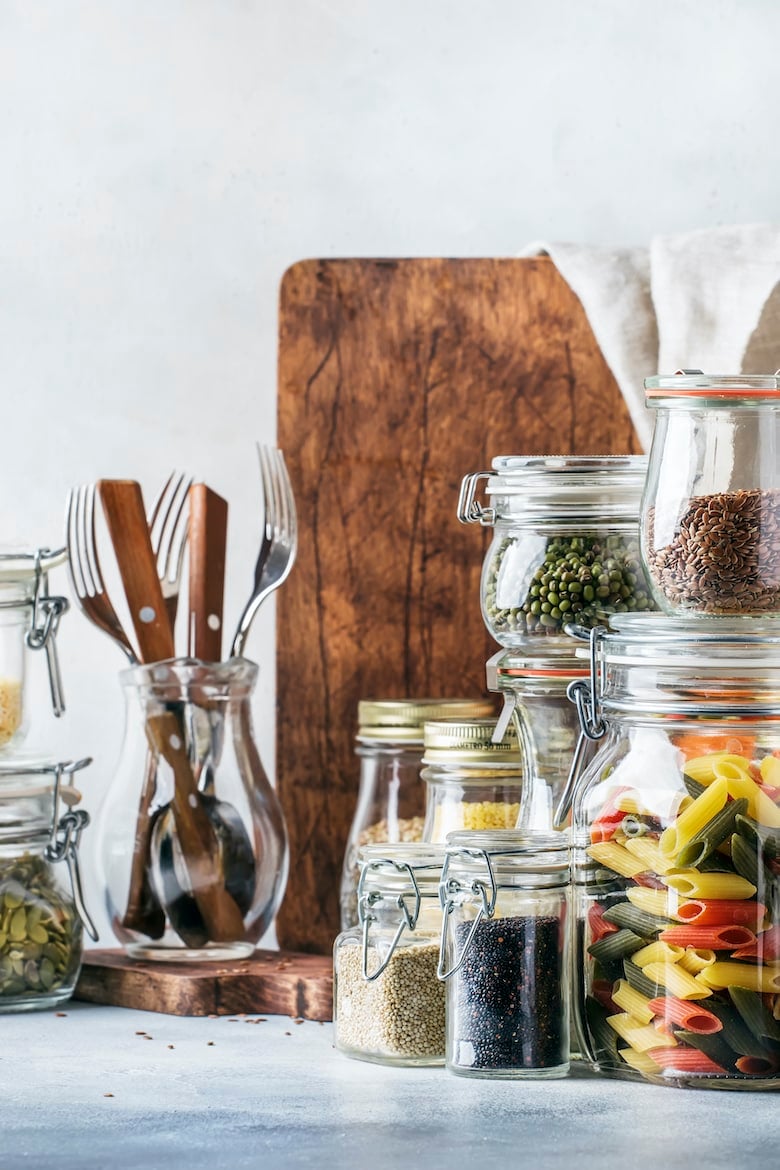 Stocks or set of cereals, pasta, groats, organic legumes and useful seeds in glass jars. Vegan source of protein and energy resources. Healthy vegetarian food. Domestic life scene. Gray kitchen table background. Selective focus