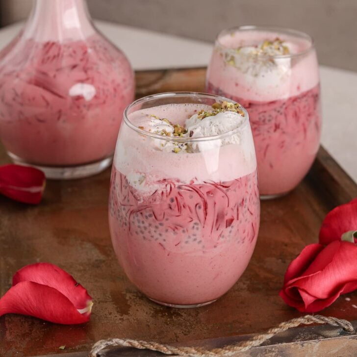 two glasses and a bottle of rose falooda in a tray with a pink rose on the side