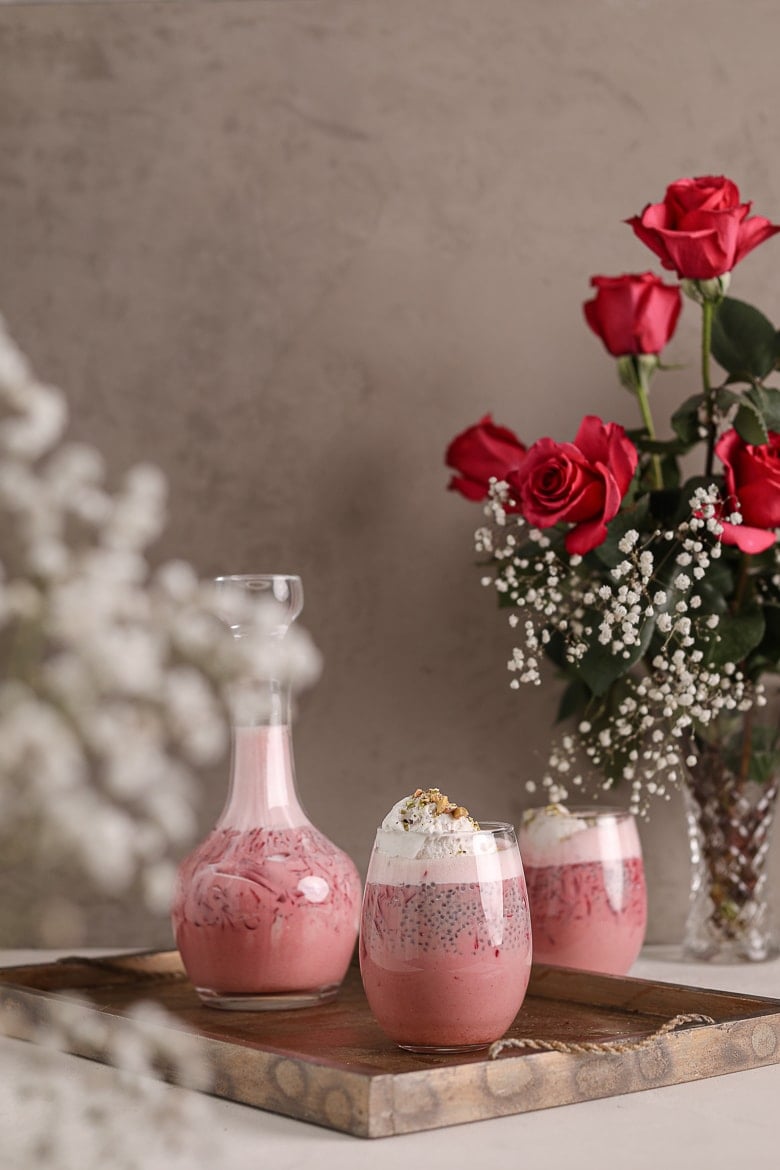 two glasses and a bottle of rose falooda in a tray with a backdrop of pink roses