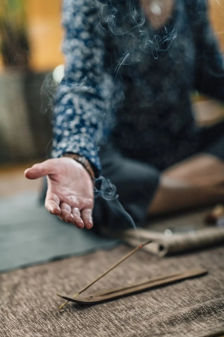 Burning incense stick with smoke and female hand with open palm during meditation at home.
