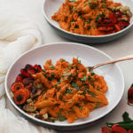 two bowls of creamy vegan pasta Indian style with a side of roasted vegetables and flowers in the foreground
