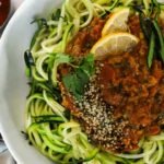 a bowl of zucchini noodles spaghetti topped with a simple curry sauce with lemon slices