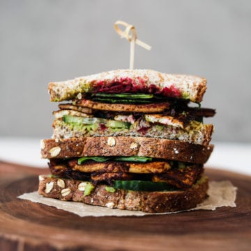 two half tofu sandwiches stacked on top of one another, filled with salad and beetroot on a wooden board