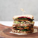 two half tofu sandwiches stacked on top of one another, filled with salad and beetroot on a wooden board