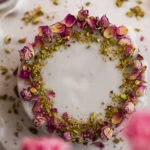 Persian love cake topped with icing and dried roses and crushed pistachios on a cake stand