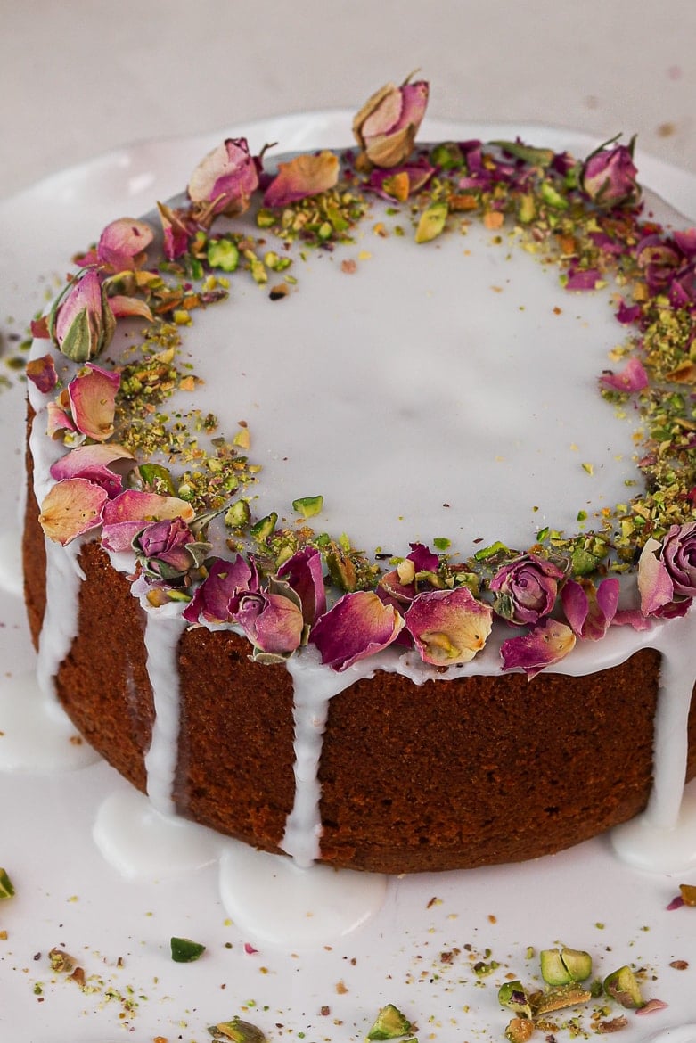 Persian love cake topped with icing and dried roses and crushed pistachios
