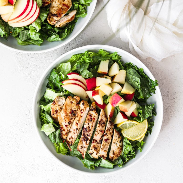 flatlay shot of a bowl of green leaf lettuce topped with spicy chicken pieces and apple chunks