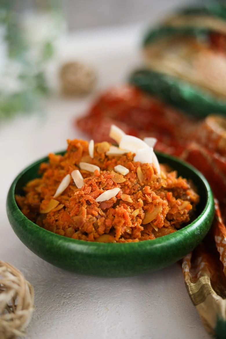 a green bowl of carrot halwa topped with almonds and coconut shavings.