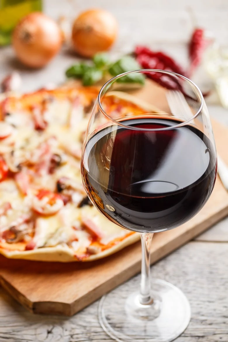 Glass of red wine, pizza on background