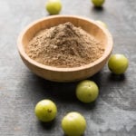 amla powder in a bowl with gooseberries all around