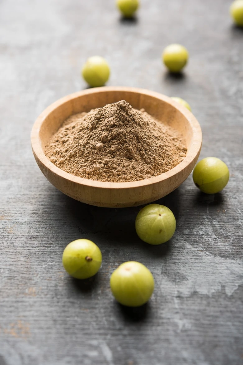 amla powder in a bowl with gooseberries all around