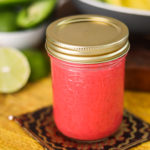 a mason jar containing raspberry salad dressing on a yellow mat with avocado in the background