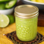 a mason jar containing avocado salad dressing on a yellow mat with avocado in the background