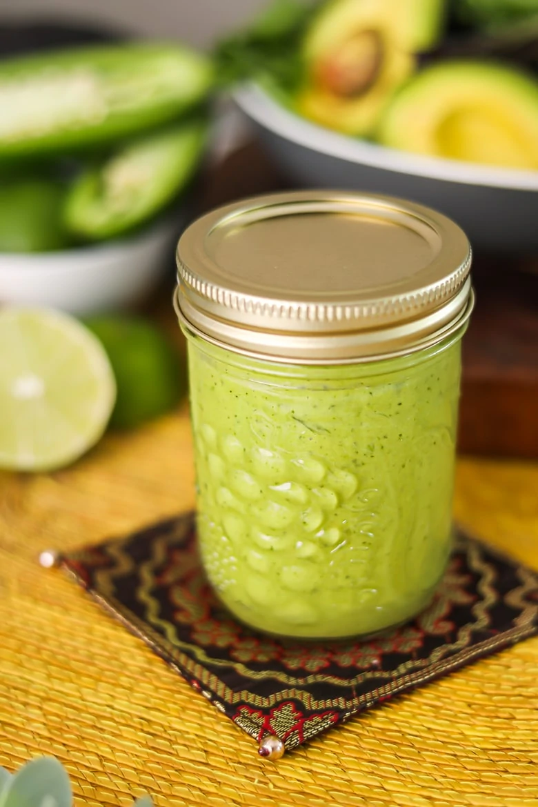 a mason jar containing avocado salad dressing on a yellow mat with avocado in the background