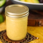 a mason jar containing honey mustard salad dressing on a yellow mat with avocado in the background