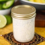 a mason jar containing raita on a yellow mat with avocado in the background