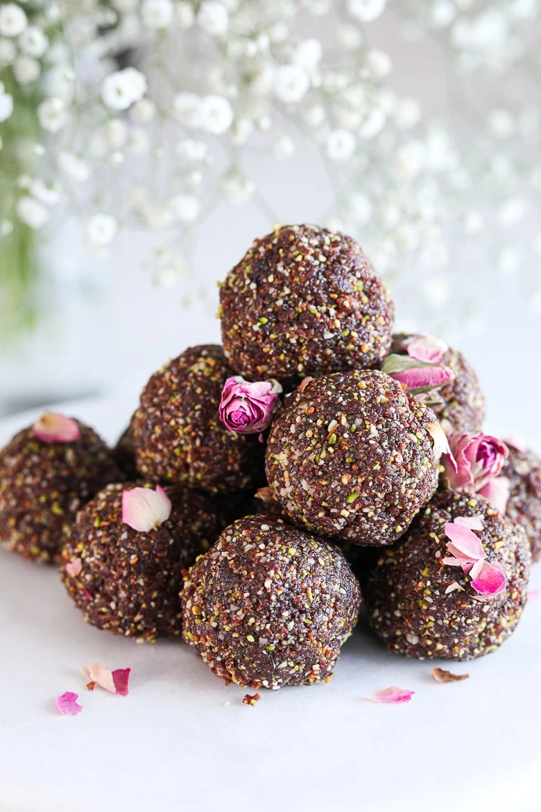 a pile of laddus - balls of Indian sweet dessert placed on a white marble cake stand sprinkled with dried roses