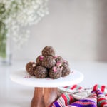 a pile of laddus - balls of Indian sweet dessert placed on a white marble cake stand sprinkled with dried roses with a traditional shawl on the countertop