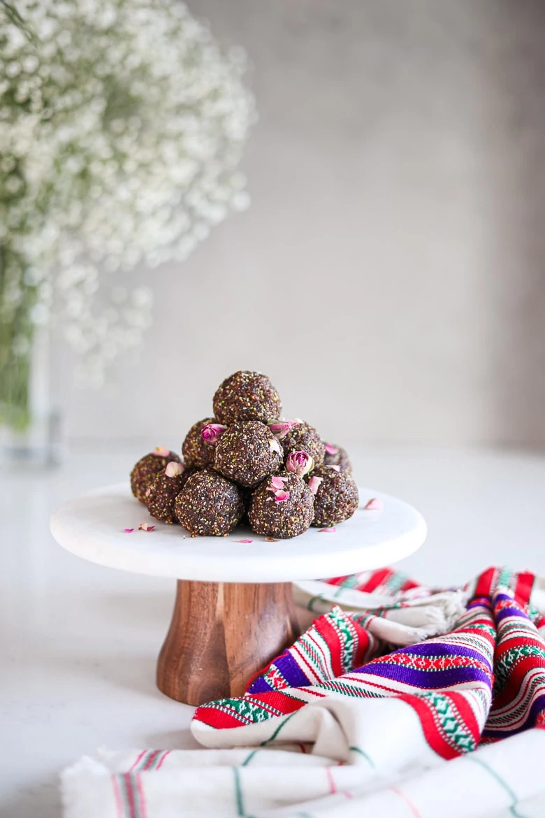 a pile of laddus - balls of Indian sweet dessert placed on a white marble cake stand sprinkled with dried roses with a traditional shawl on the countertop