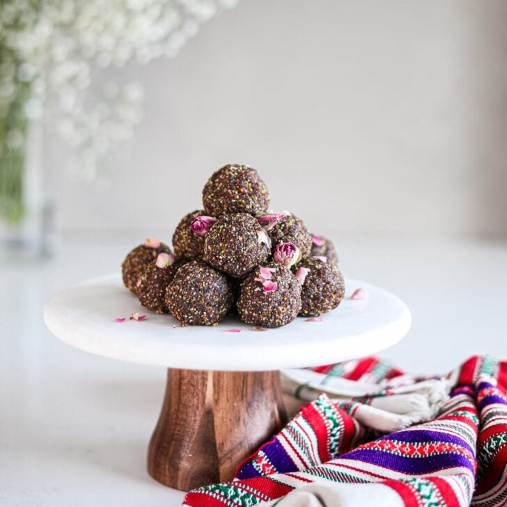 a pile of laddus - balls of Indian sweet dessert placed on a white marble cake stand sprinkled with dried roses with a traditional shawl on the countertop