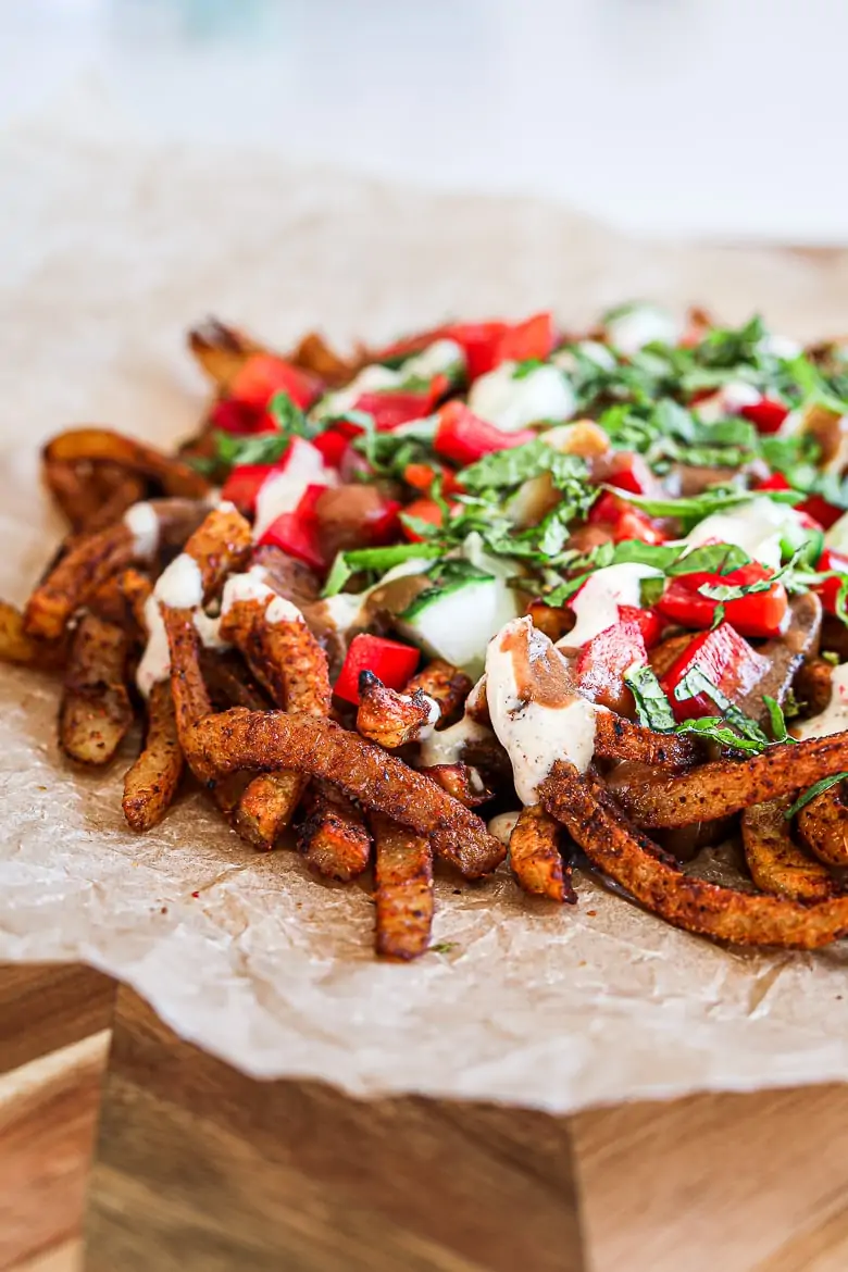 Spicy oven baked french fries loaded with peppers, cucumber and dressings with chopped herbs on a wooden board