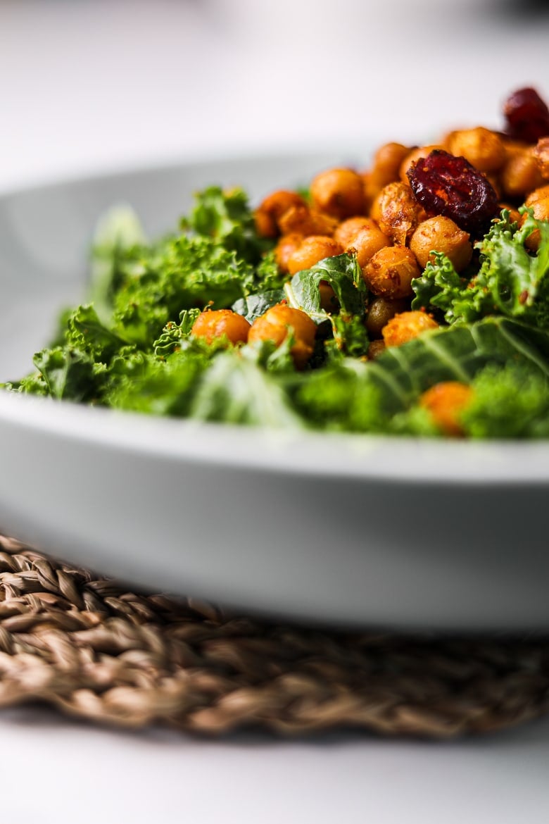perspective shot of a grey bowl of kale salad with spicy chickpeas topped with dried cranberries