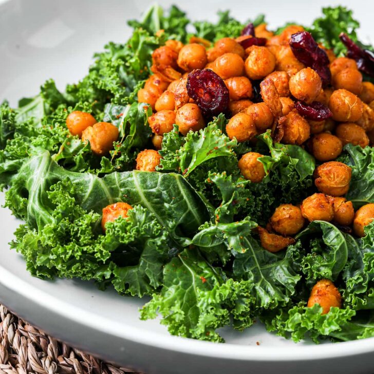 close up of kale salad topped with spicy chickpeas and dried cranberries
