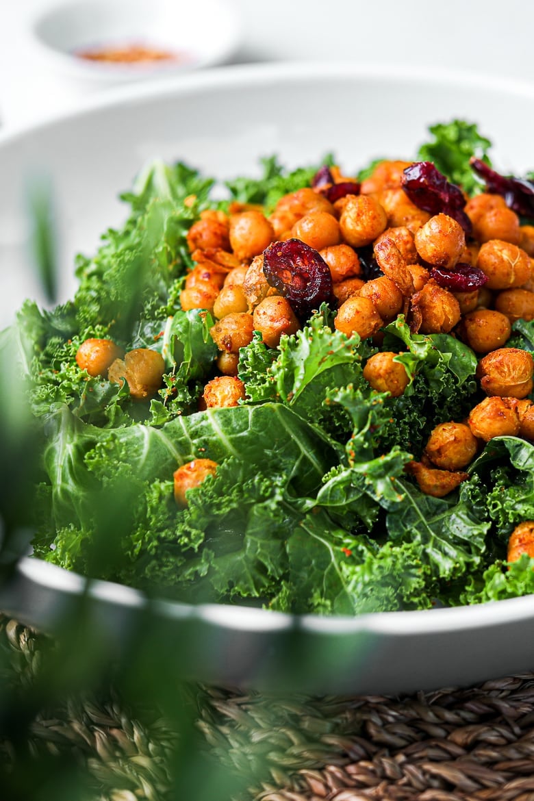perspective shot of a grey bowl of kale salad with spicy chickpeas topped with dried cranberries