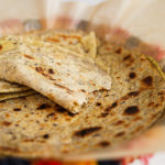 Close-up view of homemade paratha in a colourful traditional woven basket.
