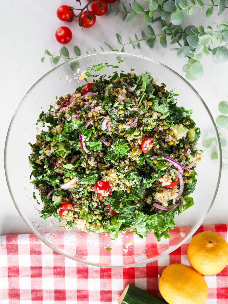 a glass salad bowl of kale and quinoa salad with tomatoes, red onion and mung beans