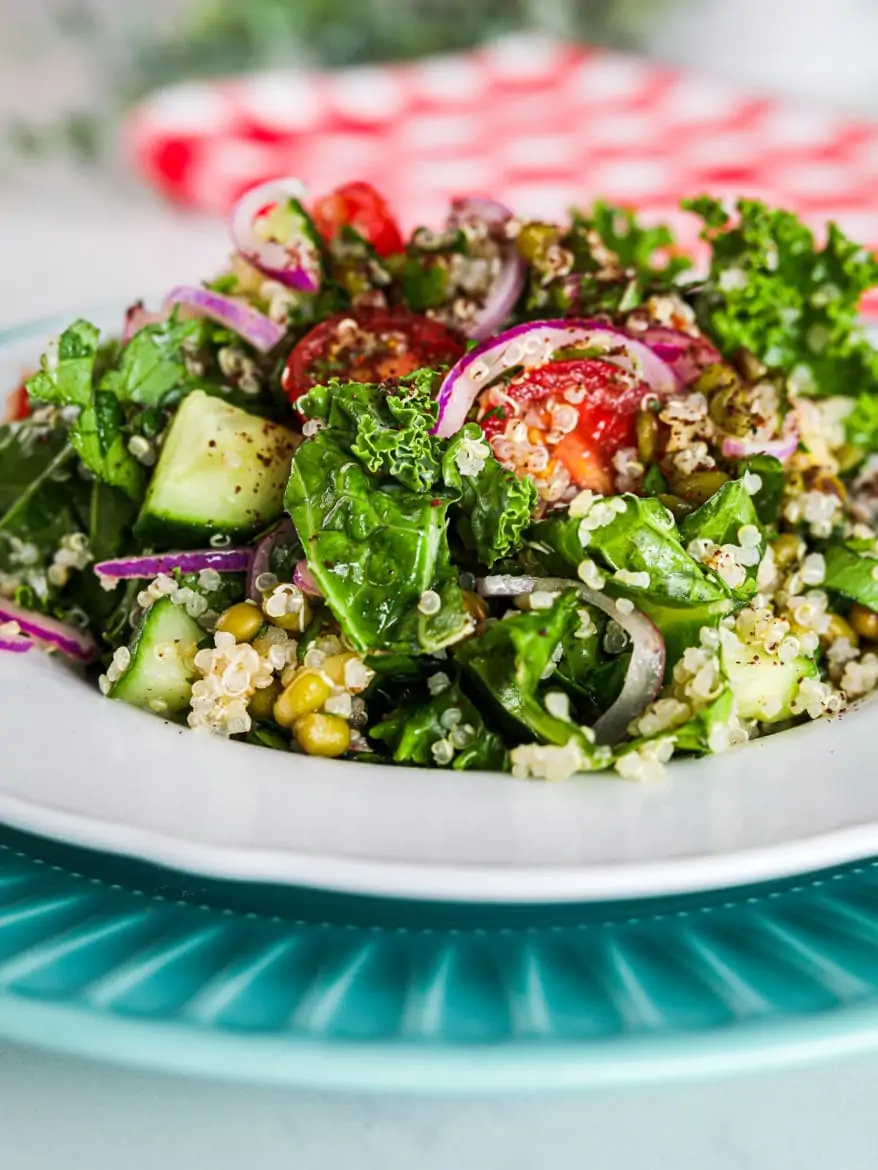 a plate of kale and quinoa salad with tomatoes, red onion and mung beans