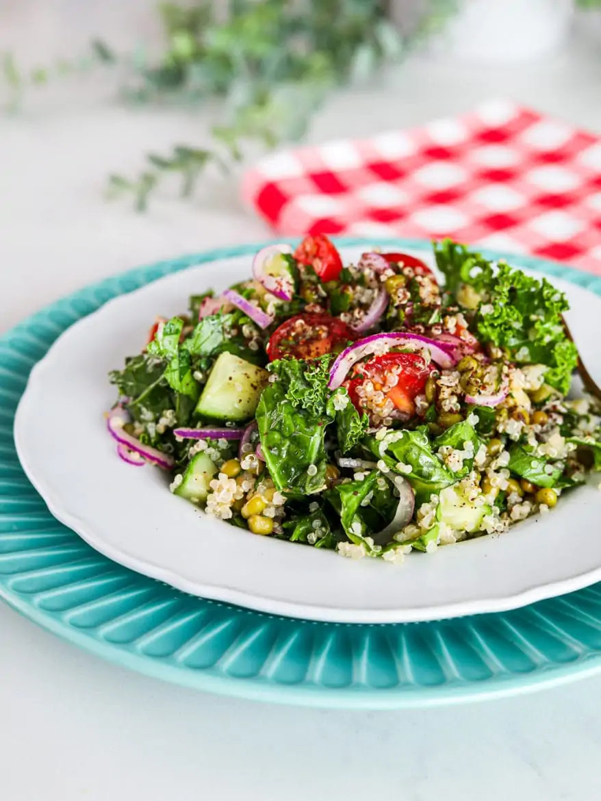a plate of kale and quinoa salad with tomatoes, red onion and mung beans