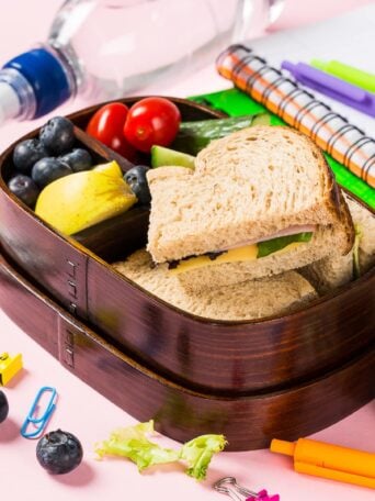 Wooden lunch box with sandwiches, vegetables and fruits on pink background and school stationery. Childrens eating concept.