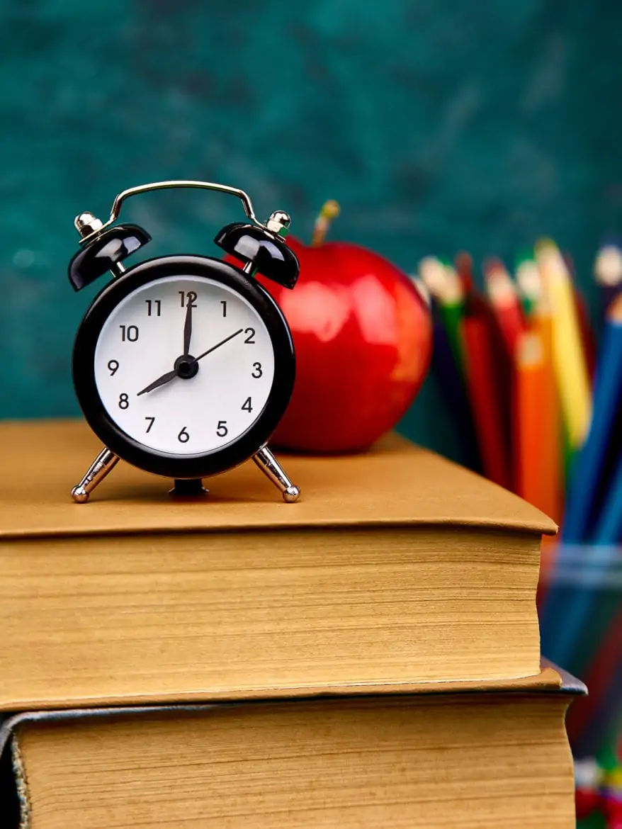Back to school supplies. Books and red apple on green background. Still life with alarm clock. Copy space.
