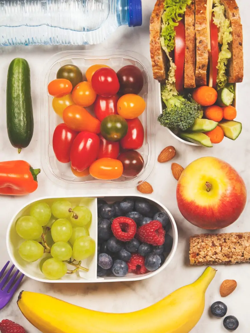 Healthy lunch box with sandwich and fresh vegetables, bottle of water and fruits on wooden background. Top view