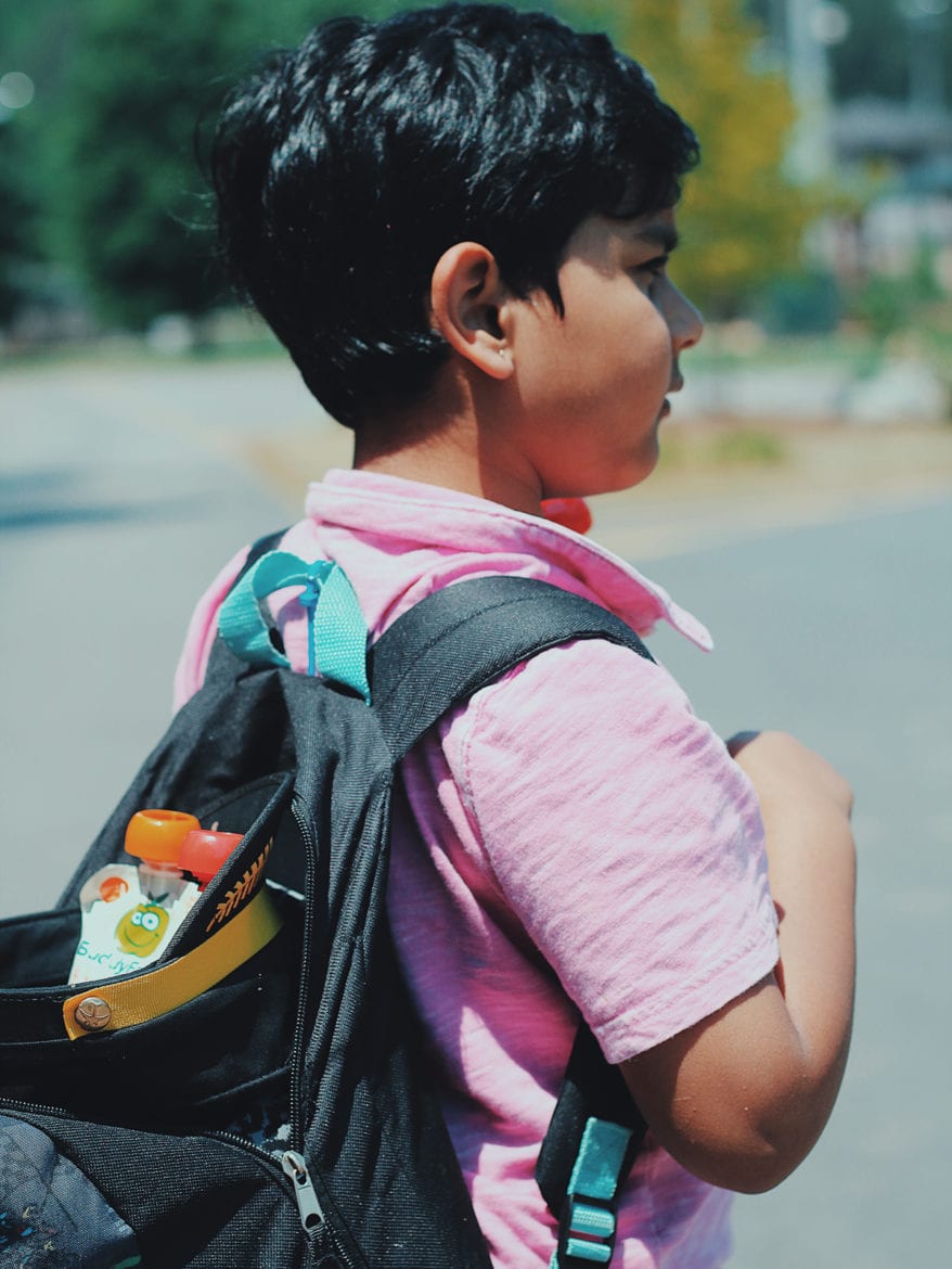 An elementary school boy with a back pack with his back to the camera