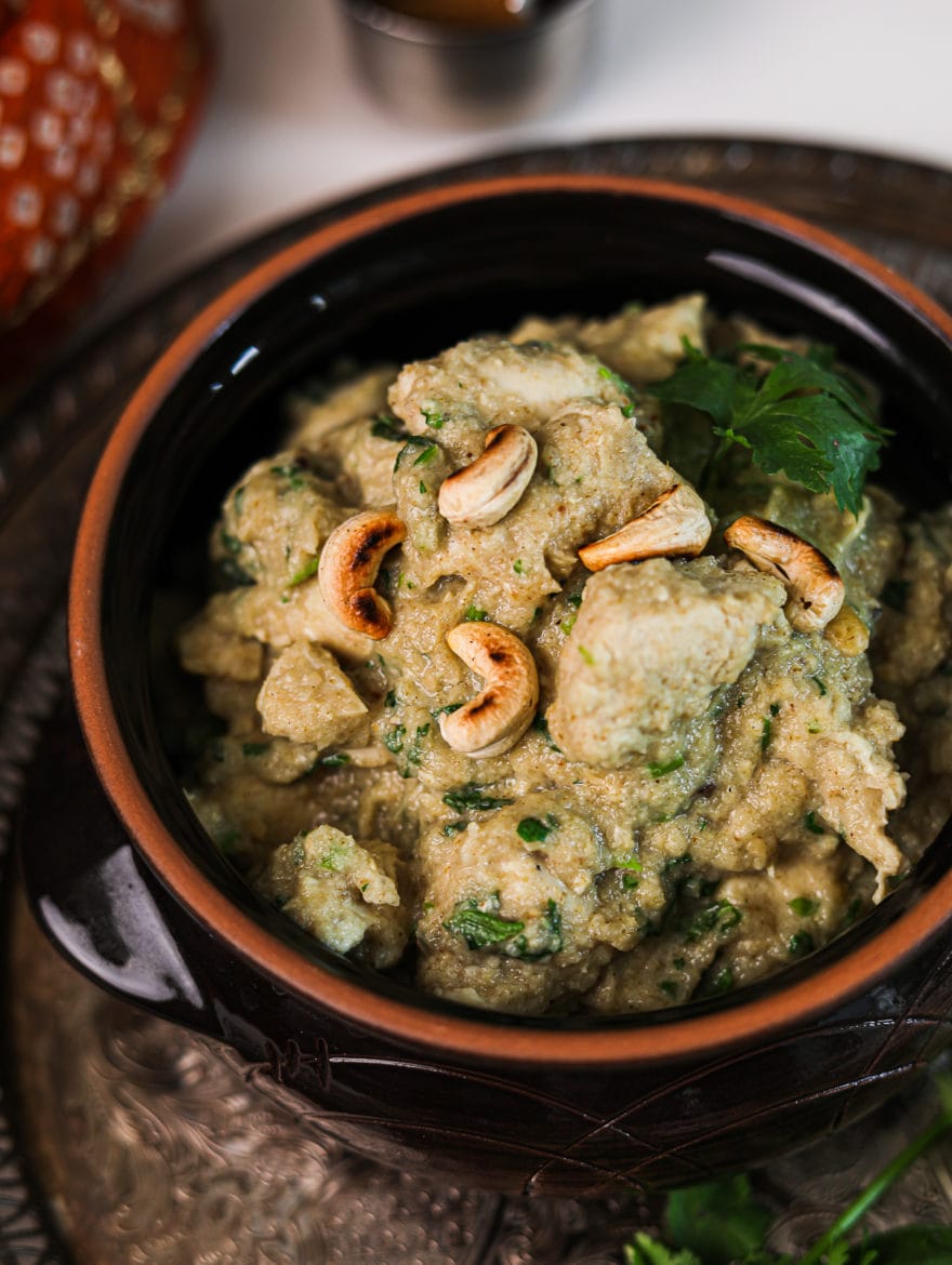 close up photo of a clay pot with chicken korma topped with toasted cashew nuts