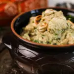 a close up image of a clay pot with chicken korma topped with toasted cashews