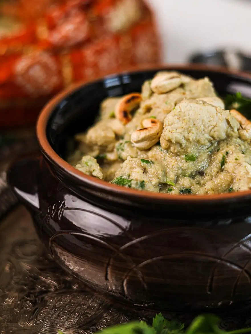 a close up image of a clay pot with chicken korma topped with toasted cashews