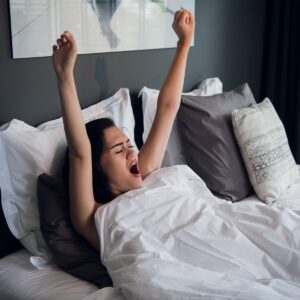 Young pretty woman yawning and stretching in comfortable bed at home