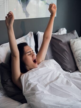 Young pretty woman yawning and stretching in comfortable bed at home