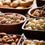 Assorted nuts and seeds in clay bowls on wooden kitchen table