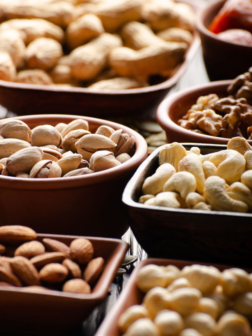 Assorted nuts and seeds in clay bowls on wooden kitchen table